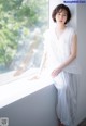 A woman sitting on a window sill in a white dress.