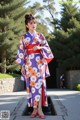 A woman in a purple and orange kimono standing in front of a fountain.