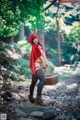 A woman in a red hooded outfit holding a basket in the woods.