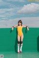 A woman in a yellow bodysuit on roller skates leaning against a green wall.