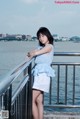 A woman in a blue dress leaning on a railing by the water.