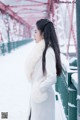 A woman in a white coat standing on a bridge in the snow.